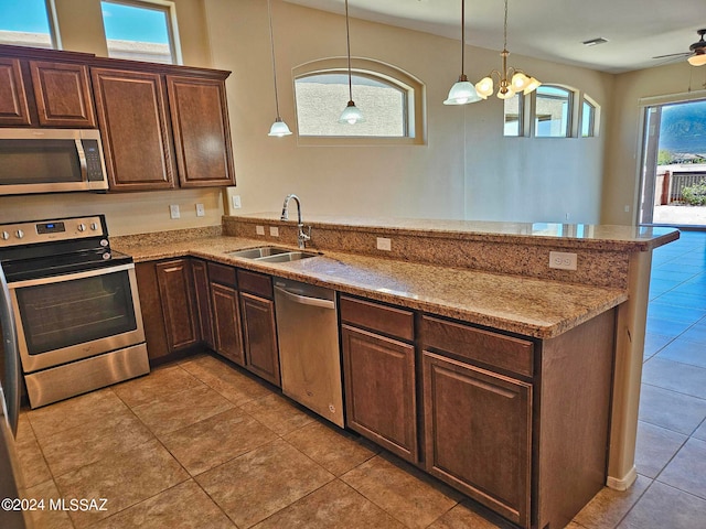 kitchen featuring light stone counters, hanging light fixtures, appliances with stainless steel finishes, a sink, and a peninsula