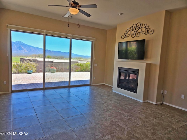 unfurnished living room featuring a ceiling fan, a glass covered fireplace, a mountain view, dark tile patterned floors, and baseboards