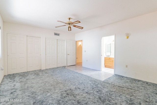 unfurnished bedroom featuring ceiling fan, light colored carpet, two closets, and ensuite bath