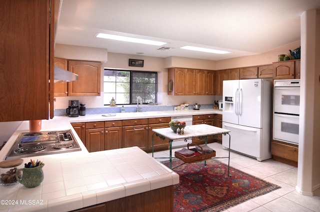 kitchen featuring tile counters, kitchen peninsula, sink, light tile patterned floors, and white appliances