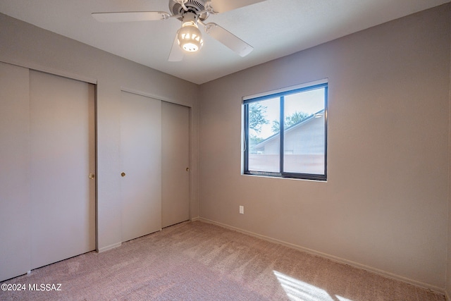 unfurnished bedroom with multiple closets, ceiling fan, and light colored carpet