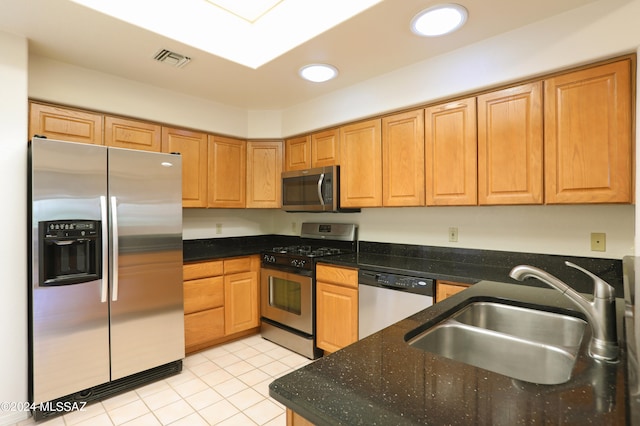 kitchen featuring light tile patterned floors, appliances with stainless steel finishes, sink, and dark stone counters