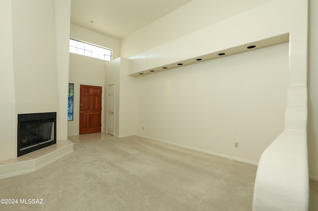 unfurnished living room with light carpet, a high ceiling, and a tiled fireplace