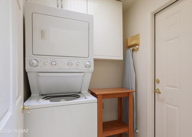 washroom featuring stacked washer and clothes dryer and cabinets