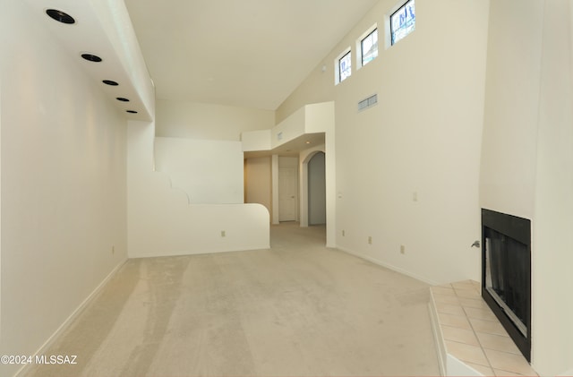 unfurnished living room featuring light carpet, high vaulted ceiling, and a tiled fireplace