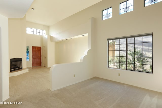 unfurnished living room featuring a high ceiling, light carpet, and a wealth of natural light