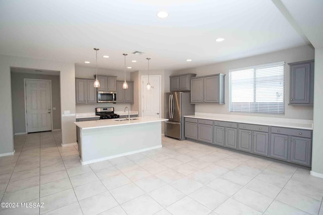 kitchen with an island with sink, hanging light fixtures, sink, gray cabinetry, and appliances with stainless steel finishes