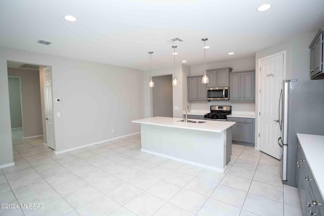 kitchen with gray cabinetry, pendant lighting, stainless steel appliances, a kitchen island with sink, and sink