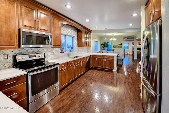 kitchen featuring kitchen peninsula, stainless steel appliances, dark wood-type flooring, sink, and decorative light fixtures