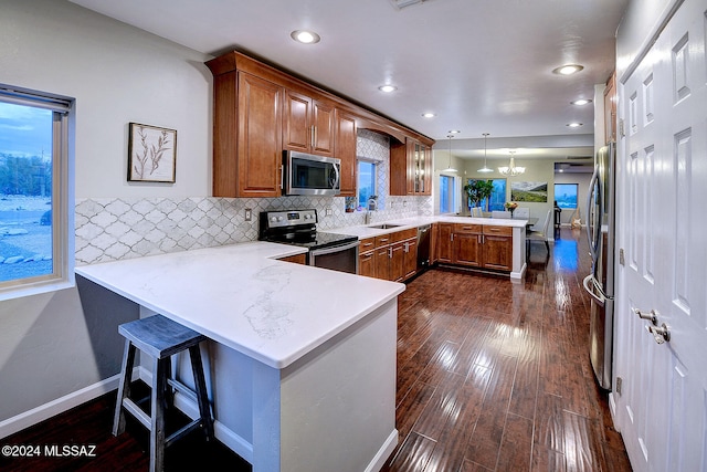 kitchen featuring kitchen peninsula, hanging light fixtures, dark hardwood / wood-style flooring, appliances with stainless steel finishes, and a breakfast bar area