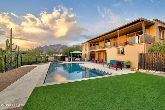 pool at dusk featuring a patio area, a mountain view, and a yard