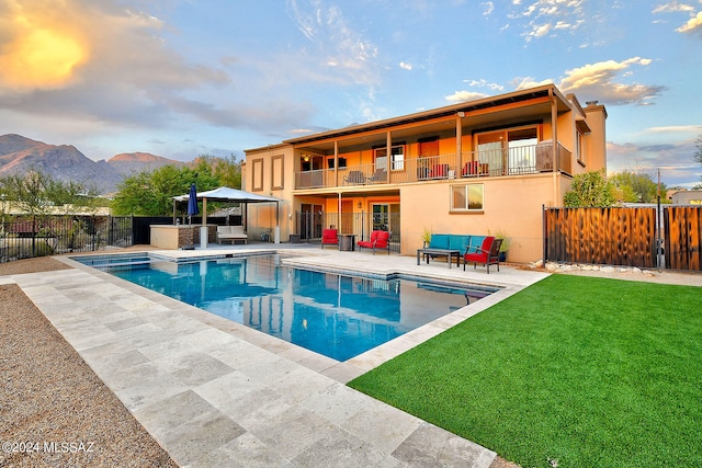 back of house featuring a patio, a fenced in pool, a mountain view, a lawn, and a balcony