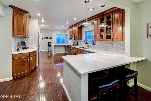 kitchen with kitchen peninsula, stainless steel appliances, sink, a breakfast bar, and dark hardwood / wood-style flooring