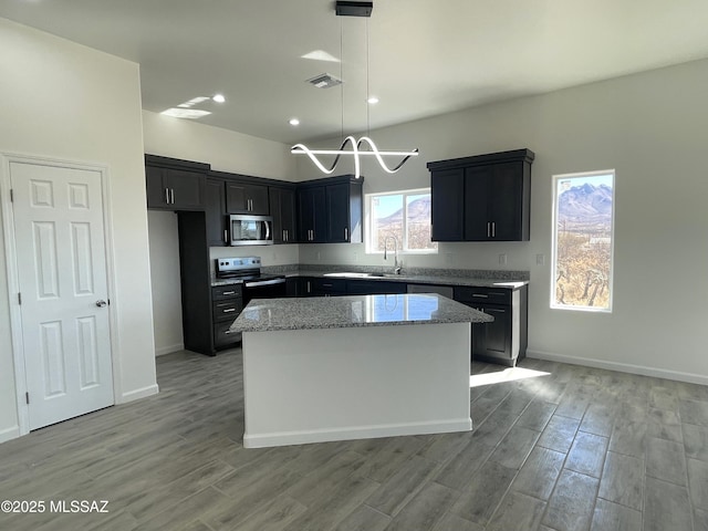 kitchen with appliances with stainless steel finishes, a center island, light hardwood / wood-style floors, hanging light fixtures, and light stone countertops