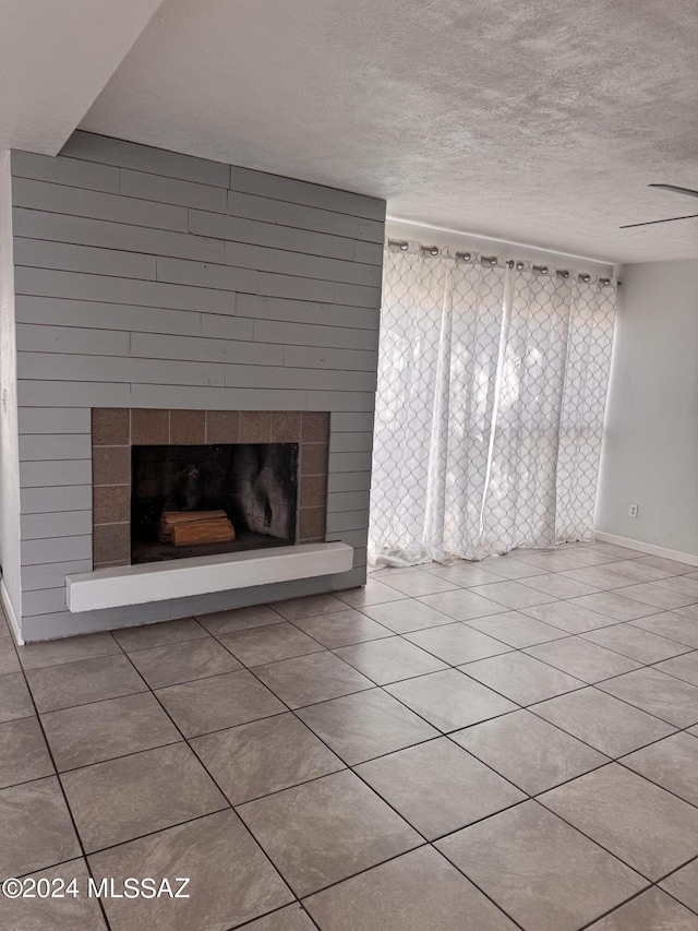 unfurnished living room with a tiled fireplace, a textured ceiling, ceiling fan, and light tile patterned flooring