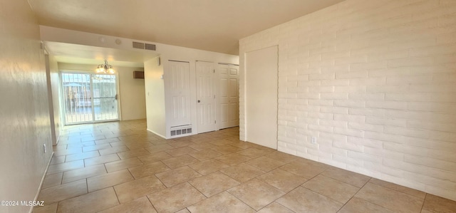 unfurnished room with brick wall, light tile patterned flooring, and a chandelier