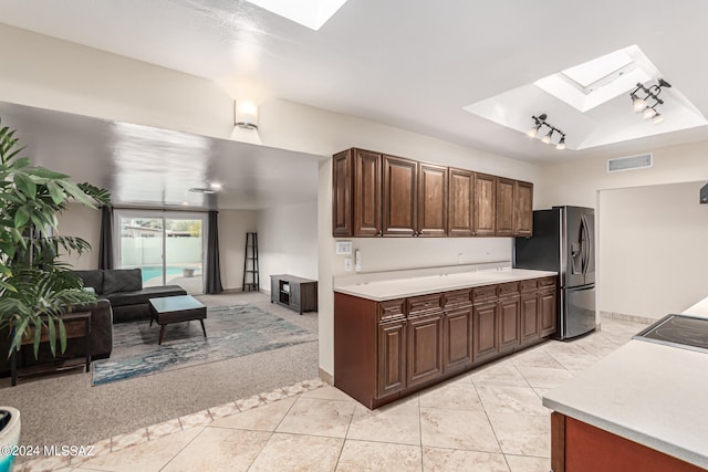 kitchen with light tile patterned floors, dark brown cabinets, stove, a skylight, and stainless steel fridge with ice dispenser