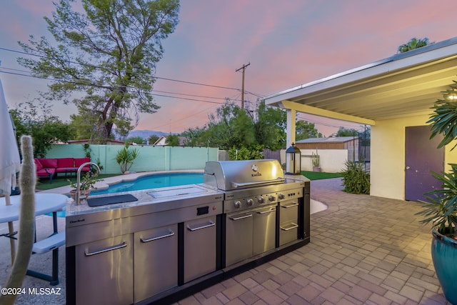 patio terrace at dusk featuring a fenced in pool, grilling area, a shed, and sink