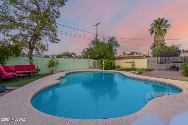 pool at dusk with a trampoline, outdoor lounge area, and a patio area