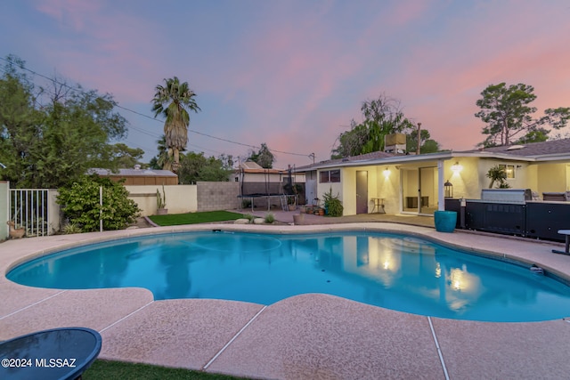 pool at dusk featuring a trampoline and a patio area