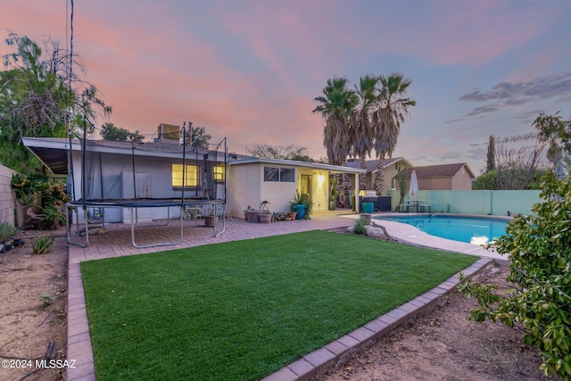 5731 E 2nd St, Tucson, AZ 85711 - back of house at dusk with a lawn, a fenced in pool, a patio area, a trampoline, and a fenced backyard