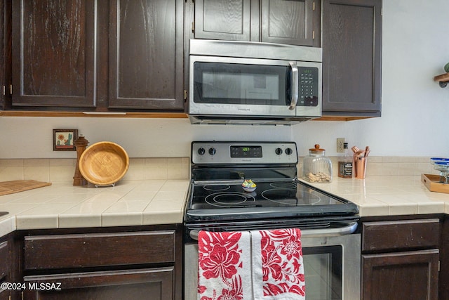 kitchen with appliances with stainless steel finishes, tile counters, and dark brown cabinetry