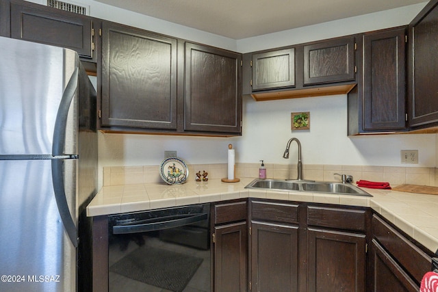 kitchen featuring stainless steel fridge, black dishwasher, dark brown cabinets, sink, and tile counters