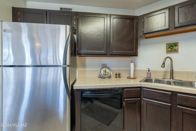 kitchen with sink, dark brown cabinets, stainless steel refrigerator, tile counters, and black dishwasher