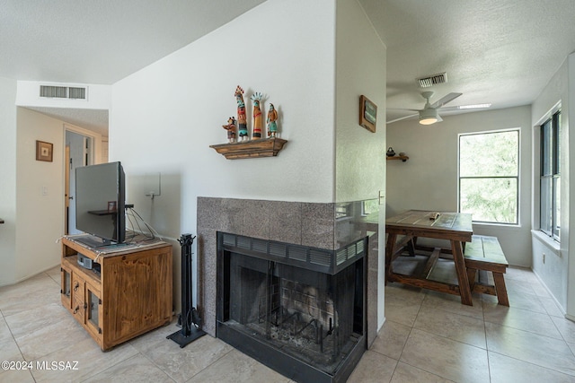 tiled living room with ceiling fan, a textured ceiling, and a tile fireplace