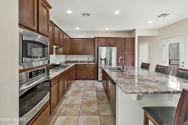 kitchen featuring light stone countertops, sink, a breakfast bar area, a center island with sink, and appliances with stainless steel finishes