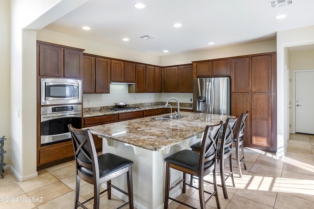 kitchen with a center island with sink, a kitchen breakfast bar, sink, light stone countertops, and stainless steel appliances