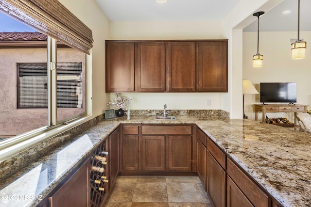 kitchen with kitchen peninsula, stone counters, sink, and pendant lighting