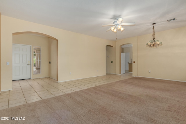 spare room featuring light colored carpet and ceiling fan with notable chandelier