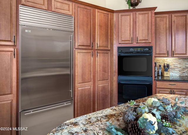 kitchen with built in refrigerator, double oven, decorative backsplash, and dark stone countertops