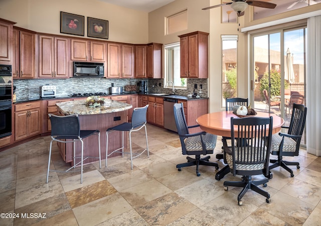 kitchen featuring sink, black appliances, a center island, dark stone countertops, and a high ceiling