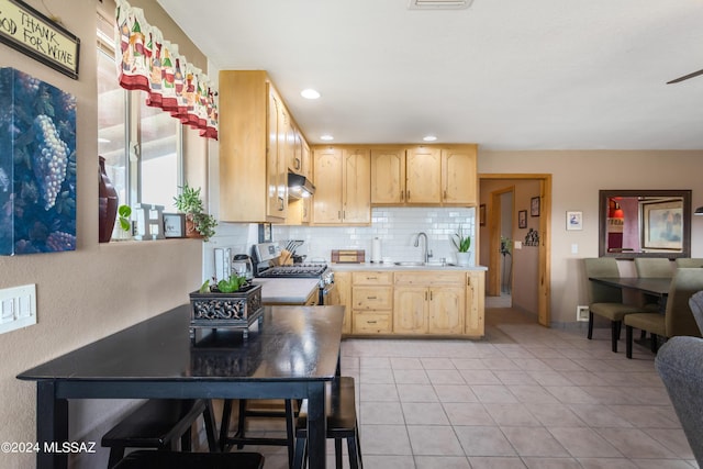 kitchen featuring light brown cabinets, gas stove, backsplash, and sink