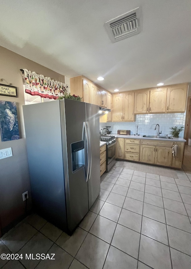 kitchen with stainless steel fridge, backsplash, light brown cabinetry, gas stove, and sink