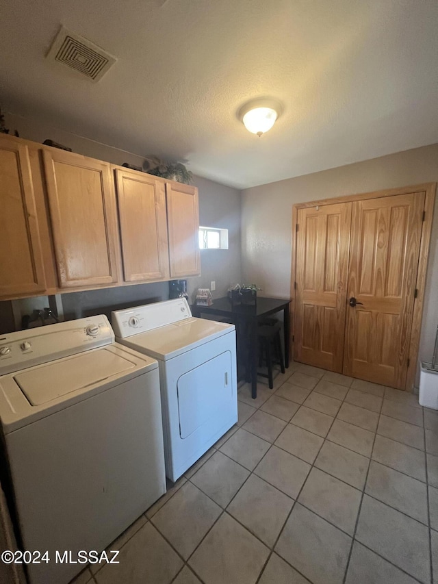 clothes washing area with cabinets, light tile patterned floors, a textured ceiling, and washer and dryer