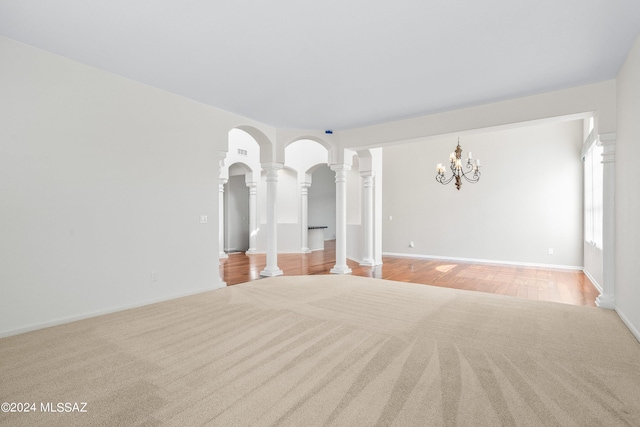 unfurnished room with a notable chandelier, light hardwood / wood-style flooring, and decorative columns