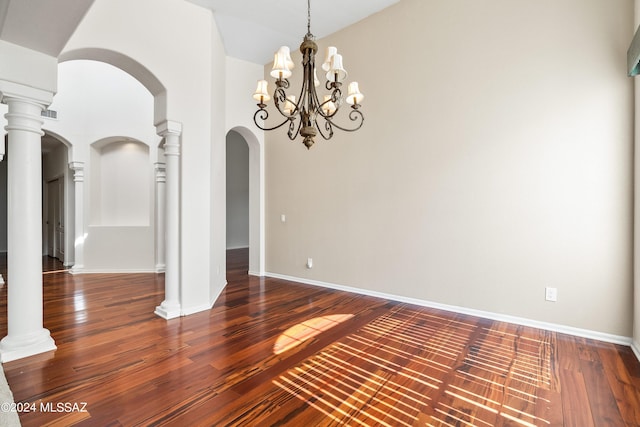 empty room with ornate columns, dark hardwood / wood-style flooring, and a notable chandelier