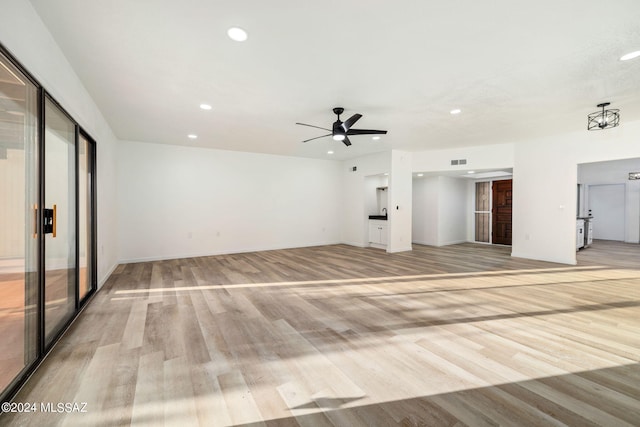 unfurnished living room featuring ceiling fan with notable chandelier and light hardwood / wood-style floors