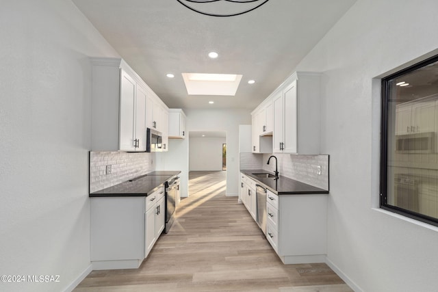 kitchen with a skylight, white cabinetry, stainless steel appliances, light hardwood / wood-style floors, and decorative backsplash