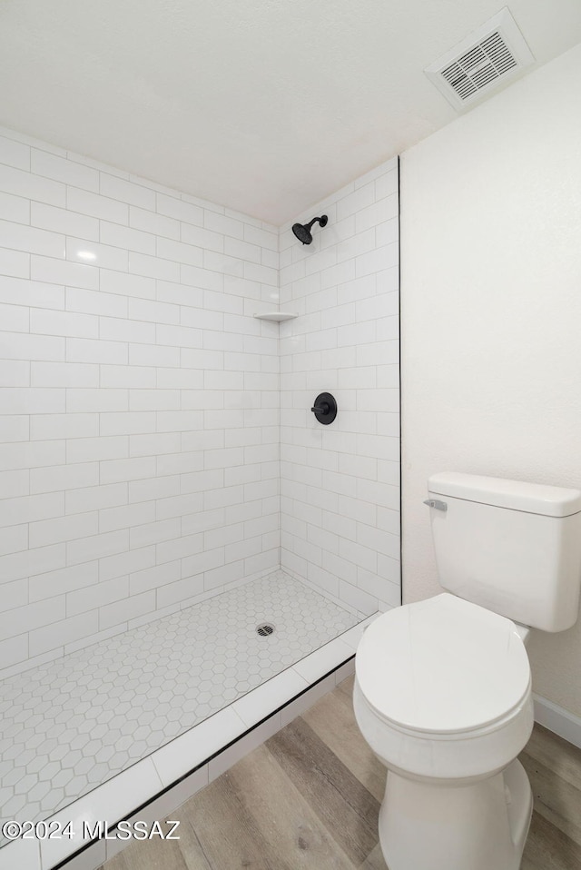 bathroom with toilet, hardwood / wood-style floors, and tiled shower