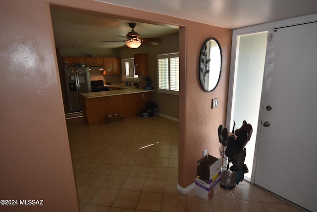 interior space featuring ceiling fan, black stove, kitchen peninsula, stainless steel fridge with ice dispenser, and light tile patterned floors