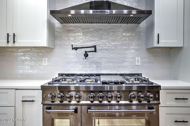 kitchen with stainless steel range, backsplash, white cabinets, and wall chimney range hood