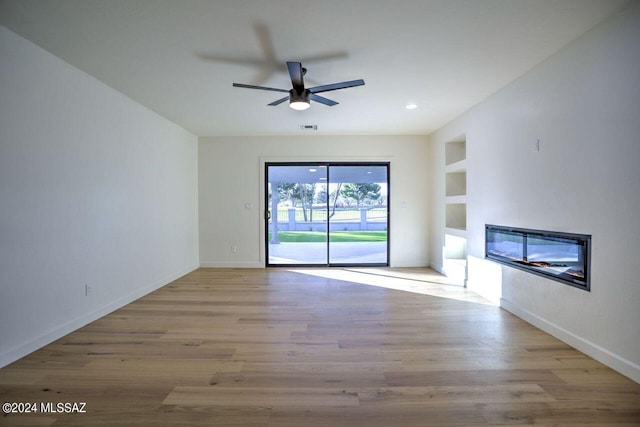 unfurnished living room with built in shelves, ceiling fan, and light hardwood / wood-style flooring