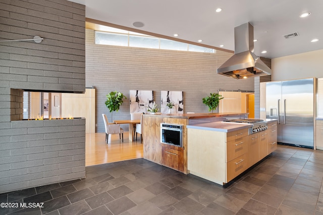 kitchen featuring brick wall, island exhaust hood, appliances with stainless steel finishes, light brown cabinetry, and a barn door