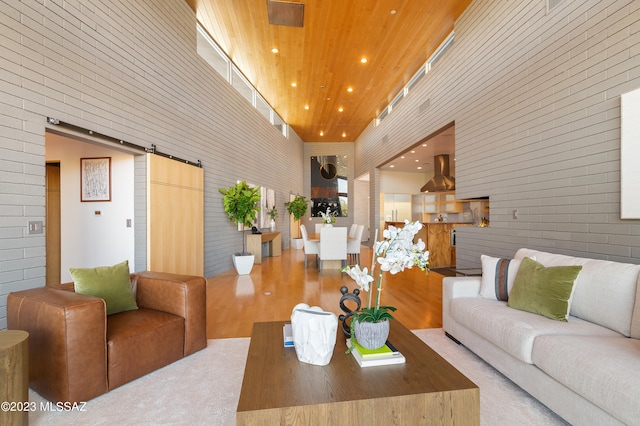 living room with a high ceiling, light hardwood / wood-style floors, wooden ceiling, and a barn door