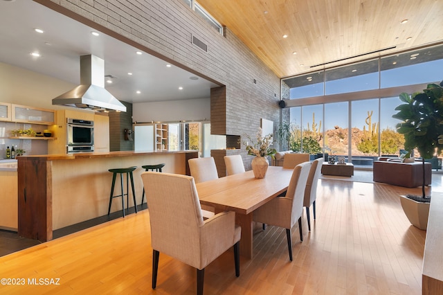 dining room featuring wood ceiling, a high ceiling, a fireplace, and light hardwood / wood-style flooring