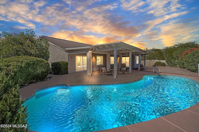 pool at dusk with a patio area and a pergola